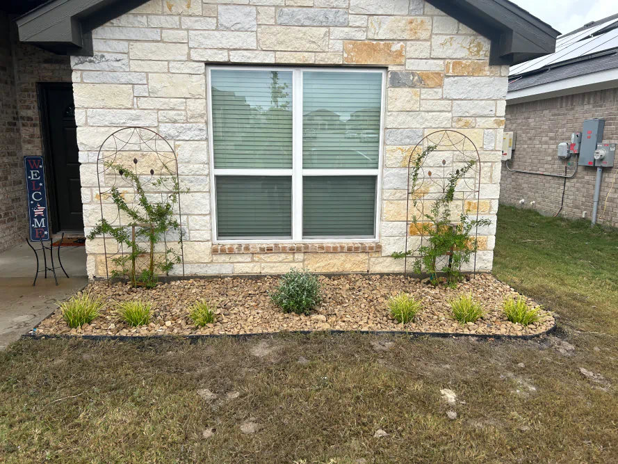 Front of a stone house with a large window and a small landscaped garden bed.