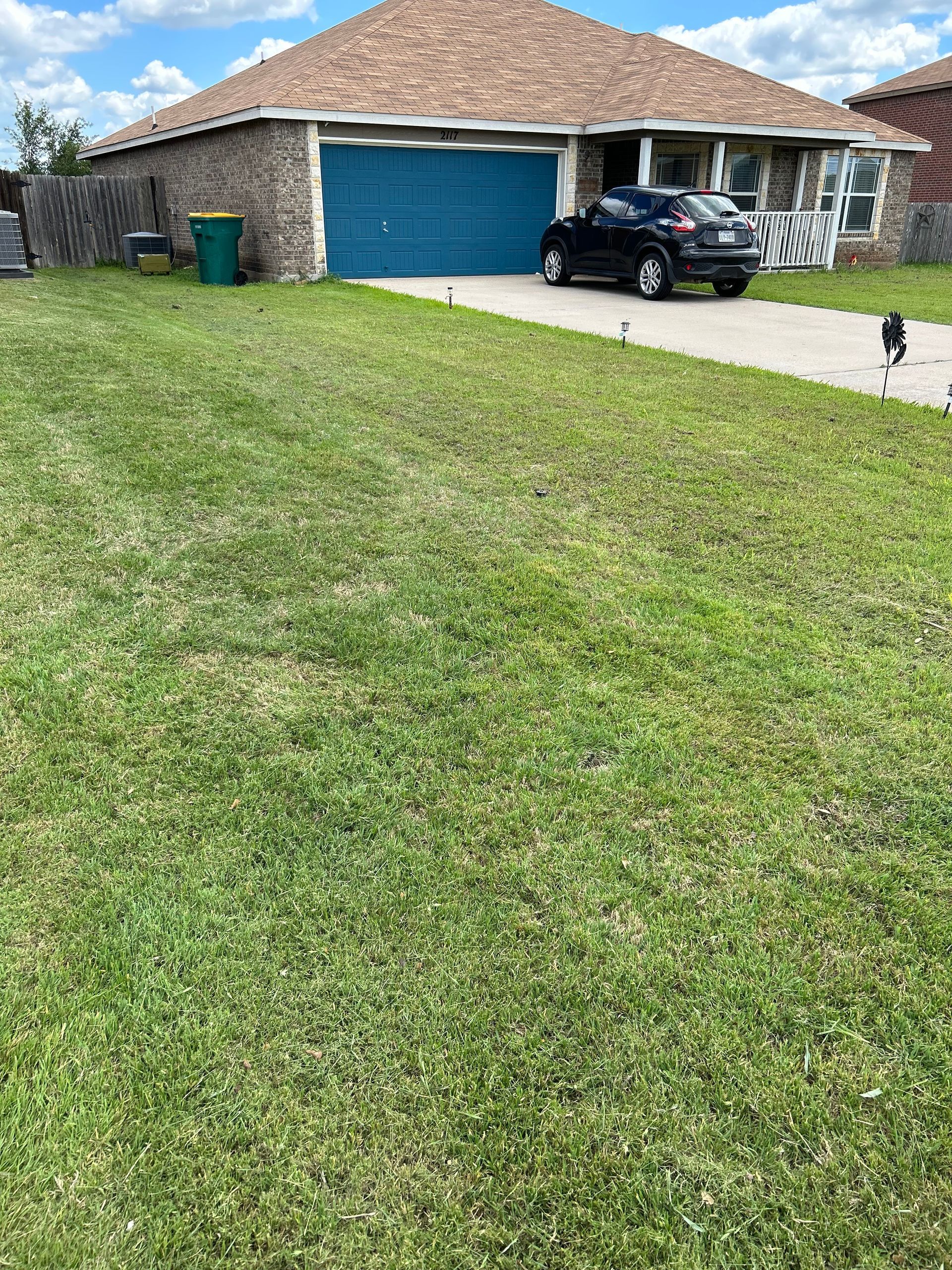 Suburban house with blue garage doors, green lawn, and a black car parked in the driveway.