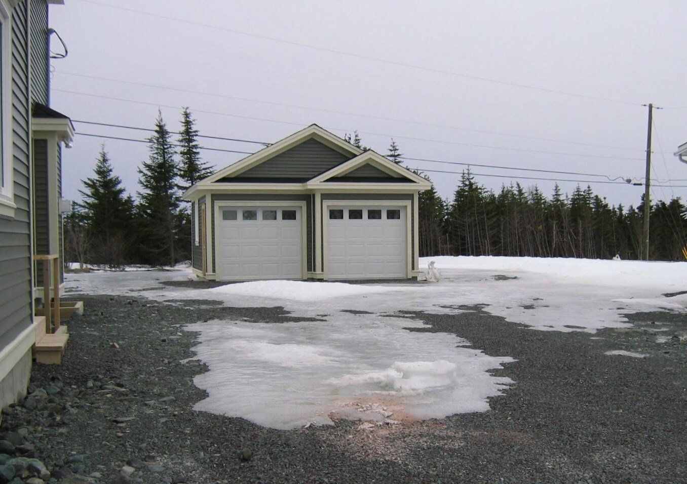 A garage with two white garage doors is surrounded by snow