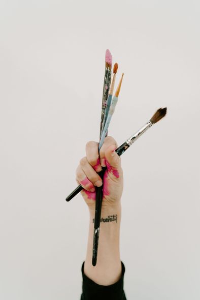 Hand holding several paintbrushes with colorful paint on the bristles and fingers