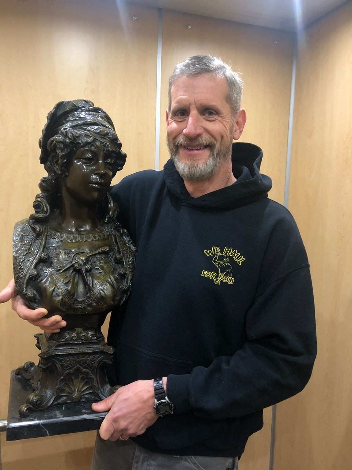 Man holding a bronze bust of a woman, against a wood-paneled wall.