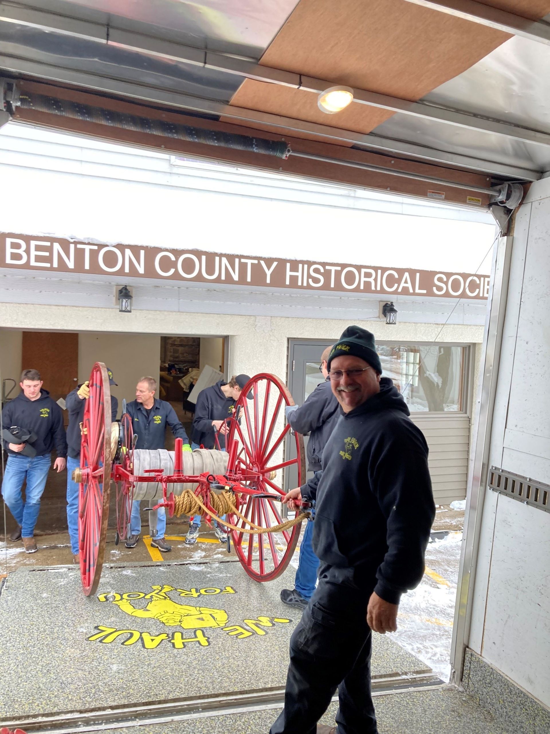 Men with historic fire wagon at Benton County Historical Society. Smiling man in black jacket.