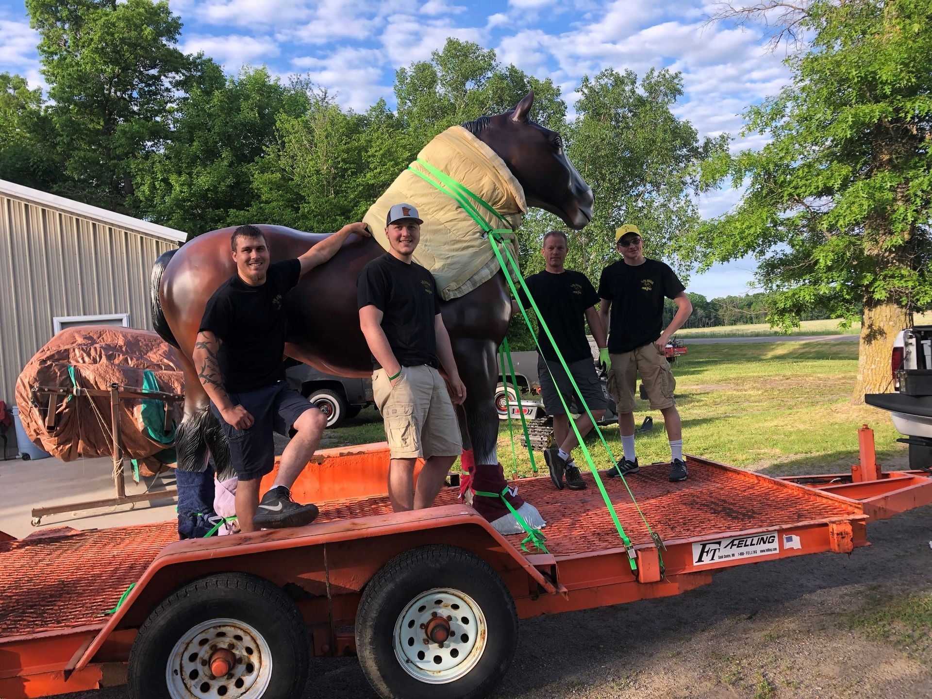 Four people pose with a bronze horse sculpture secured to an orange trailer.