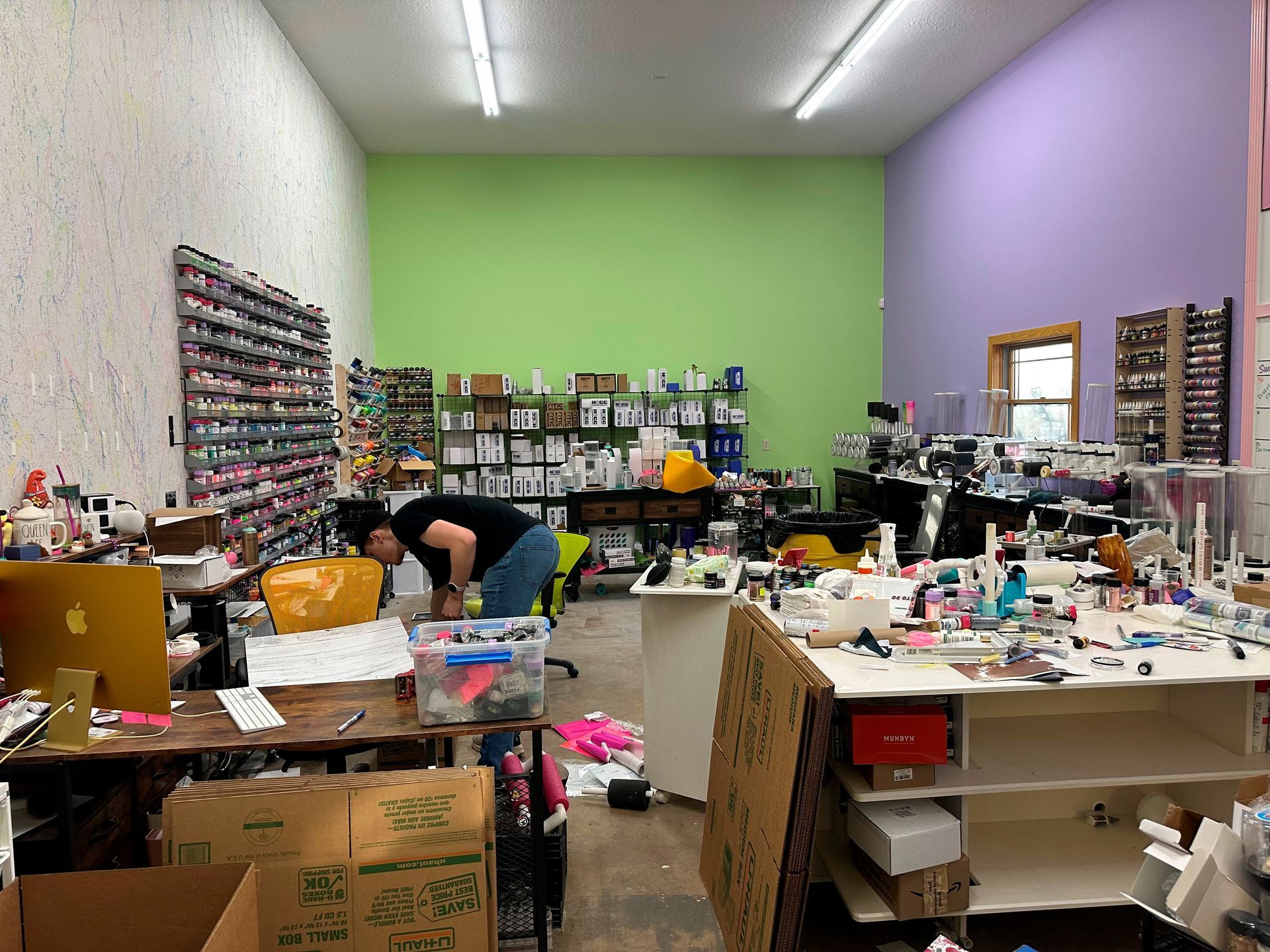 Person in cluttered workshop, green and purple walls, shelves filled with items.