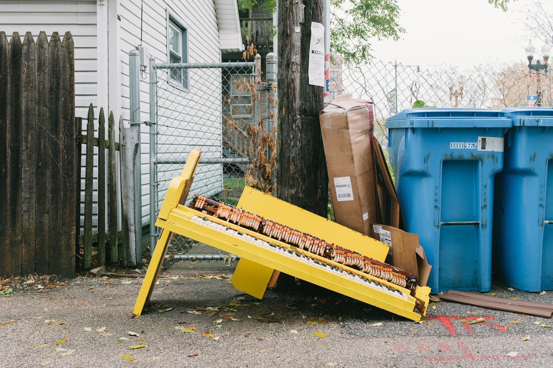 a  broken yellow piano sitting by the trash can outside