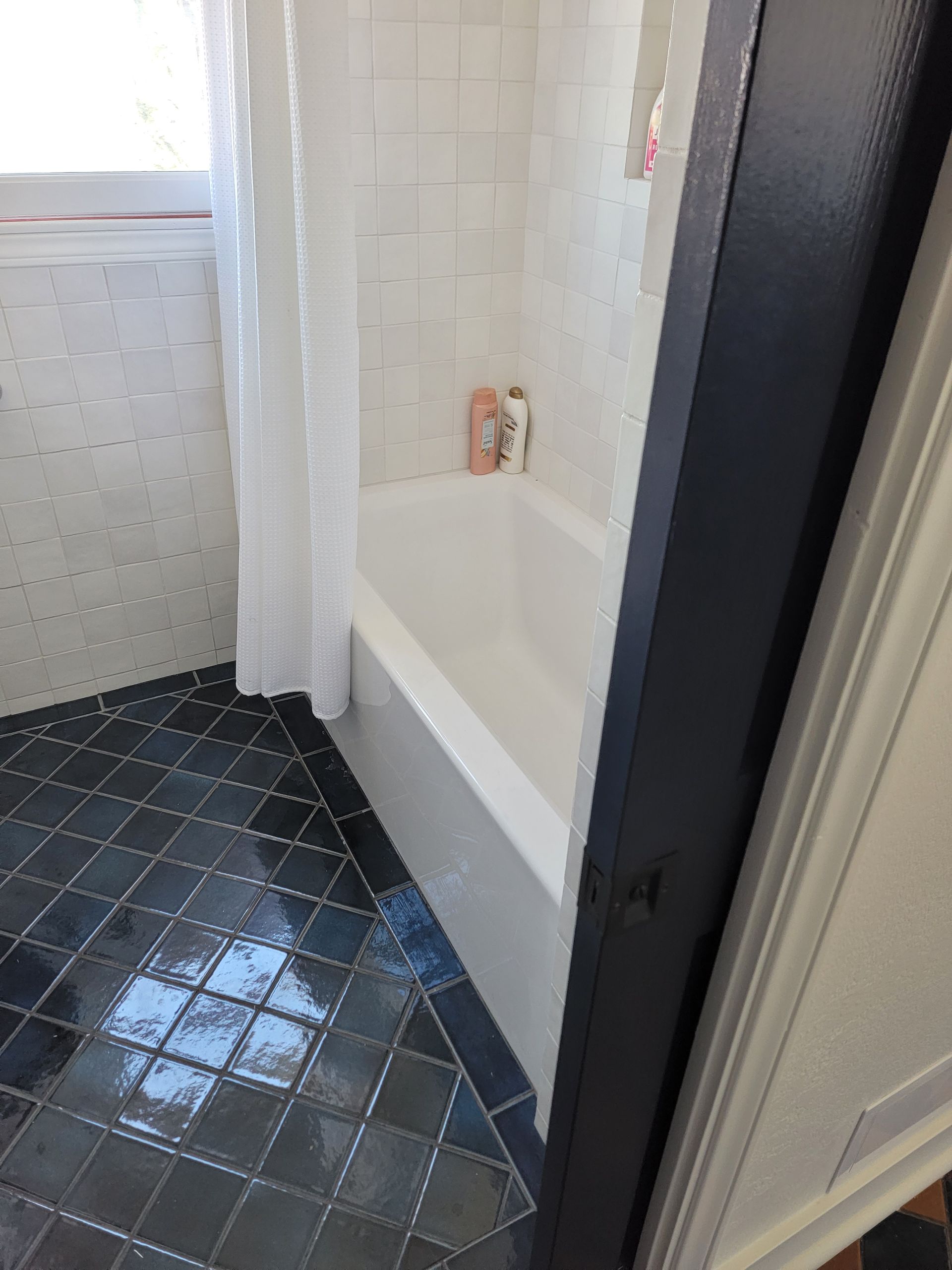 Bathroom with white tub, white tile walls, blue diamond tile floor, and black door frame.
