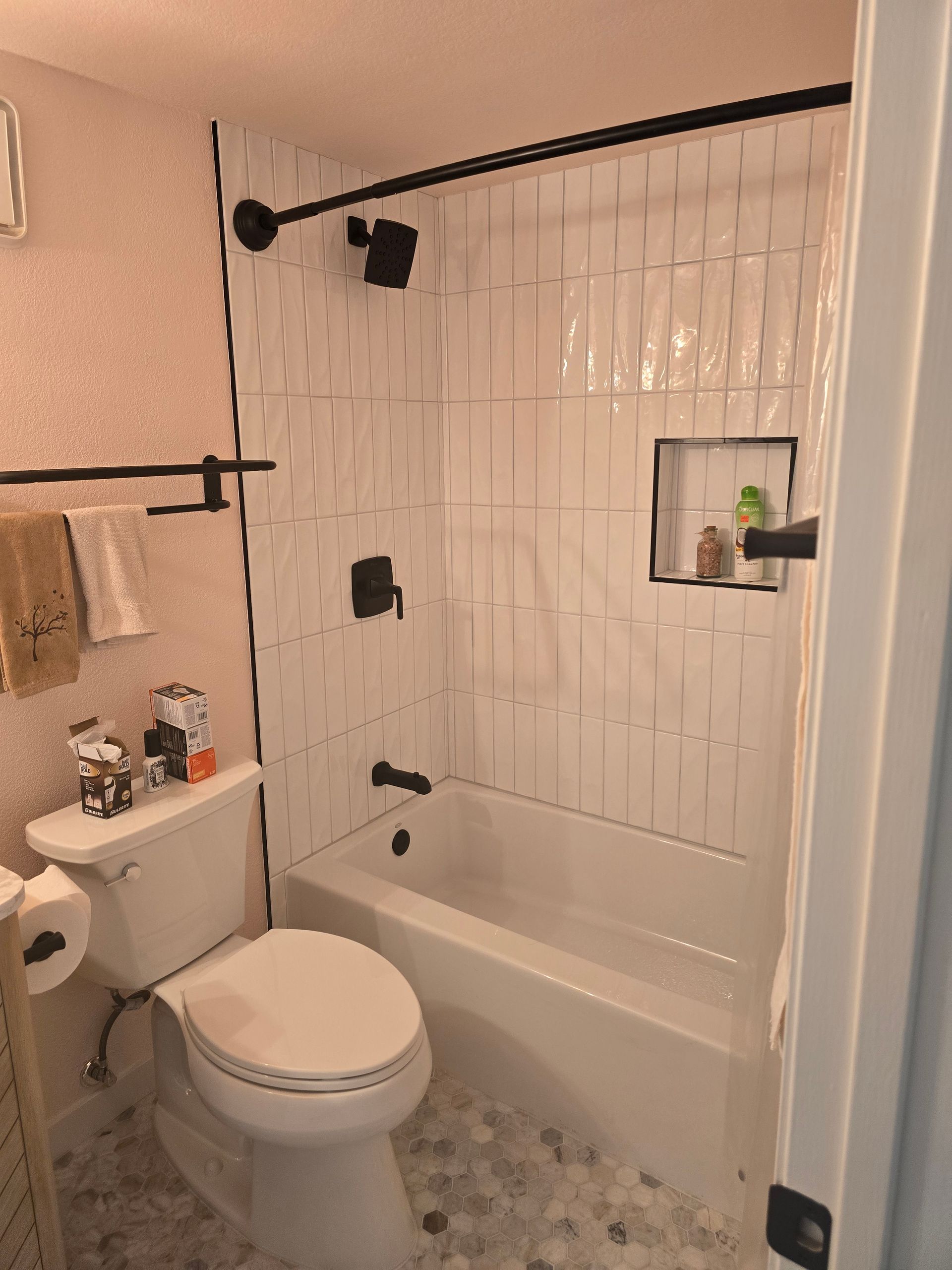 A small bathroom with white vertical tiled shower walls, black fixtures, and a white toilet.