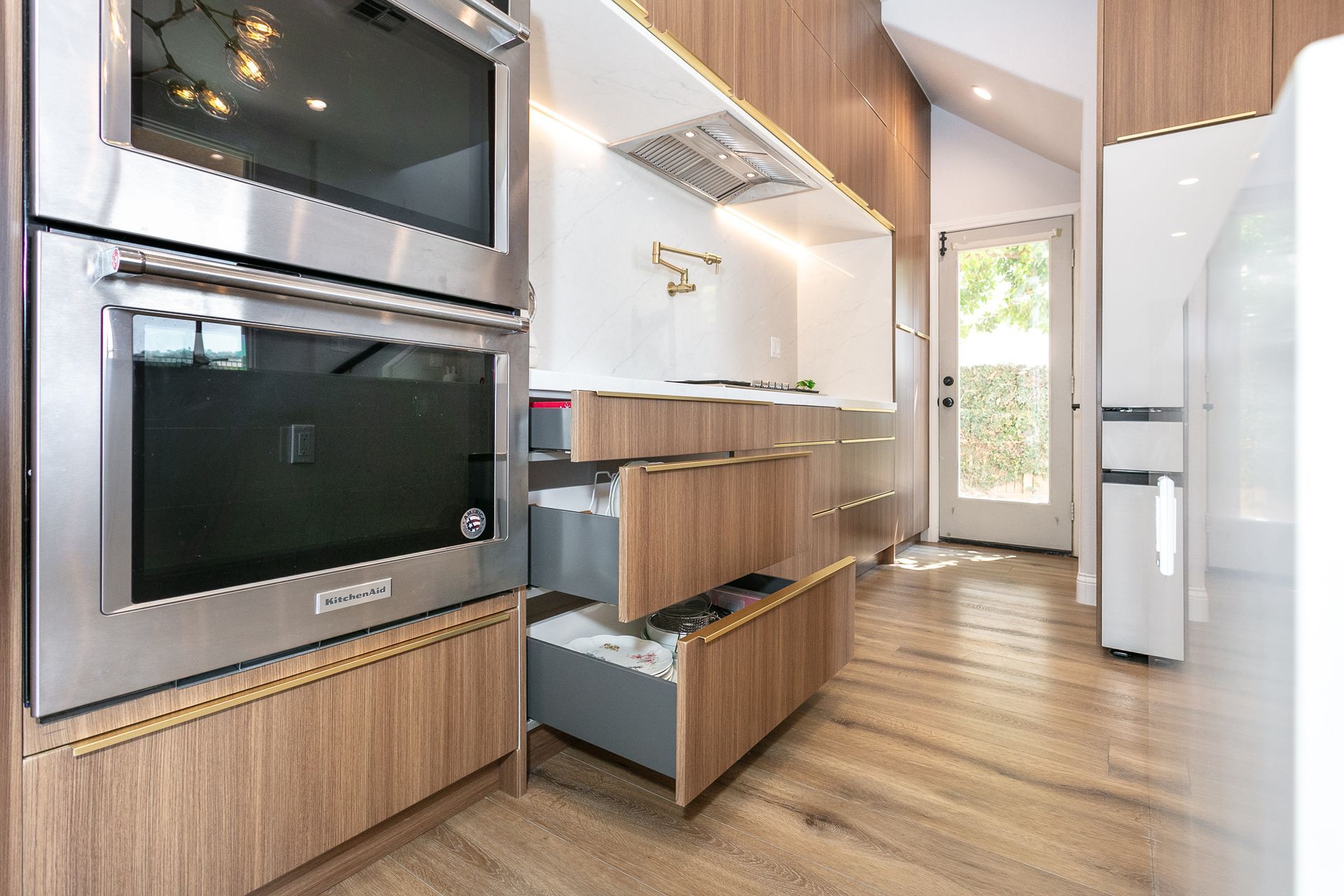 Modern kitchen with wood cabinets, stainless steel appliances, and open drawers.