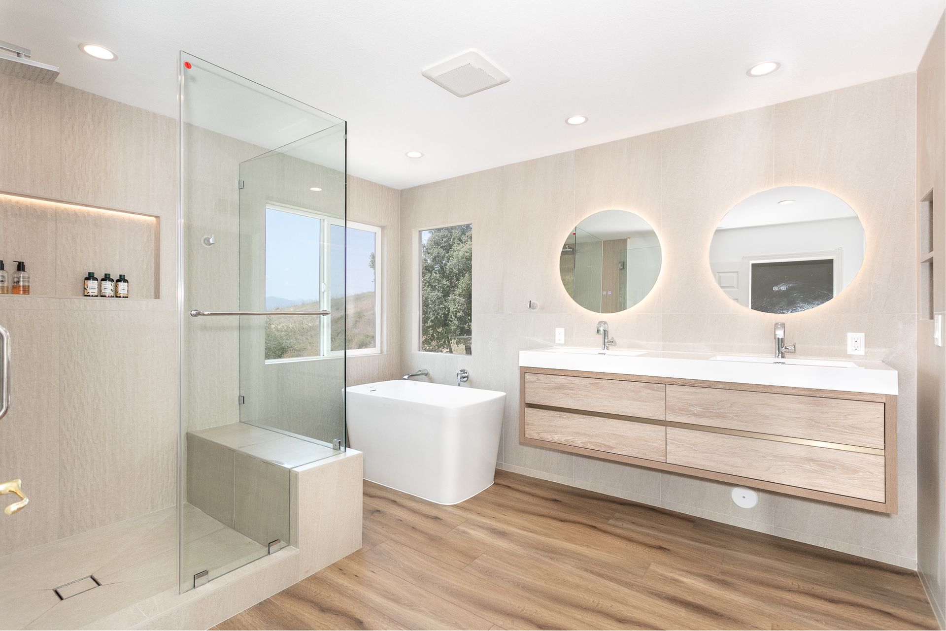 Modern bathroom with glass shower, soaking tub, double vanity, and wood-look flooring.