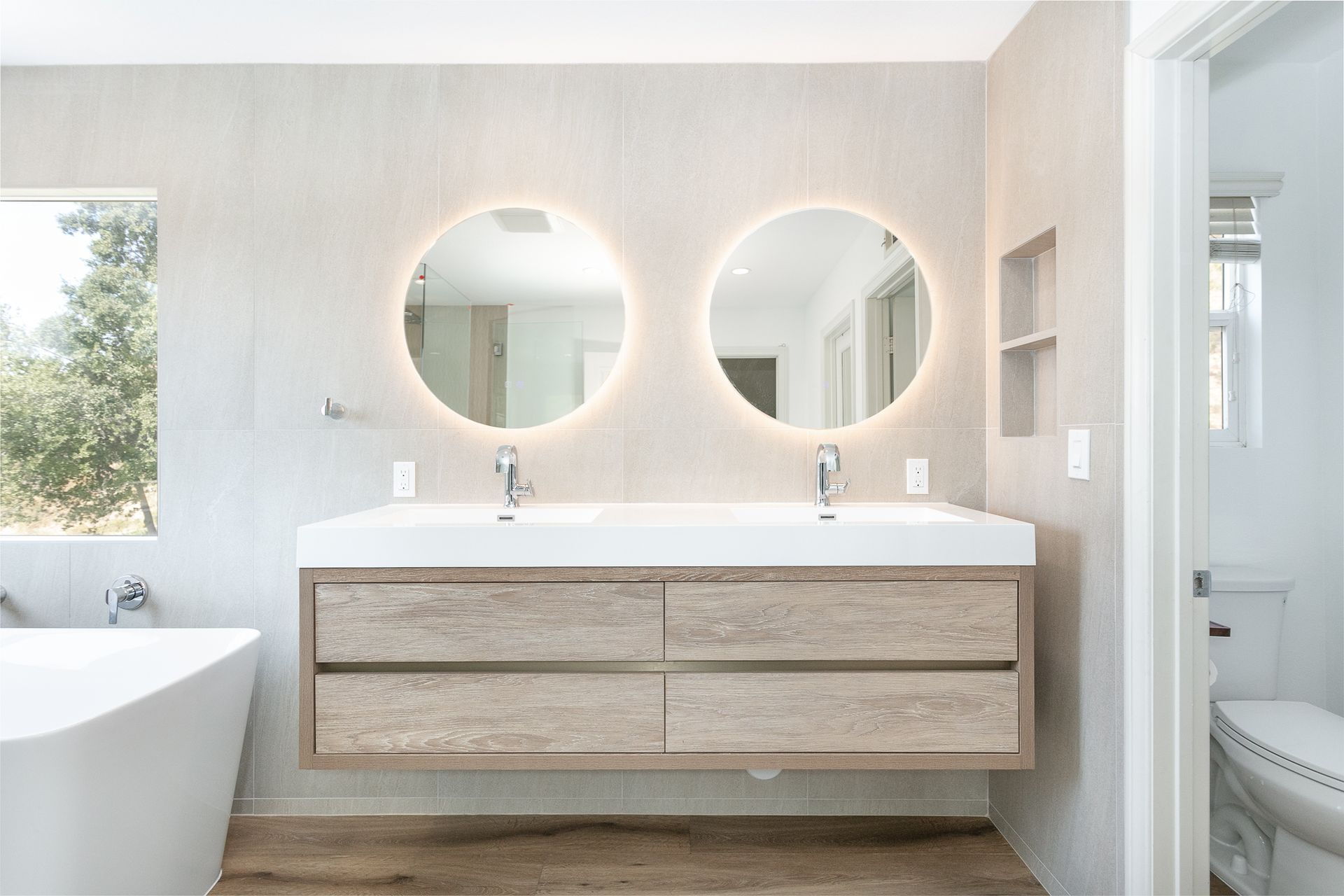 Modern bathroom with a double vanity, two round mirrors with glowing lights, and a bathtub.