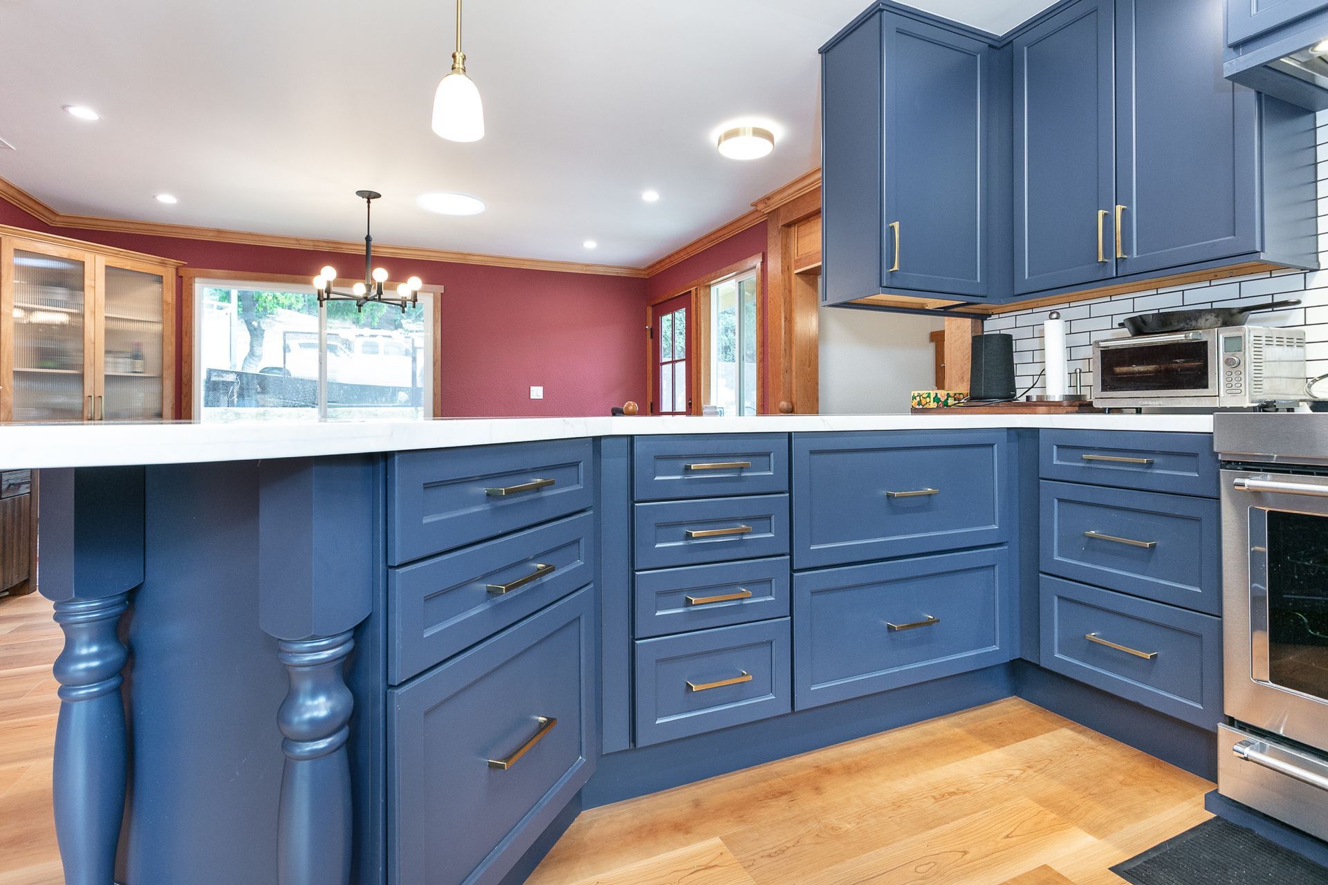 Blue kitchen cabinets with white countertop and wood floor. Dining area in background.