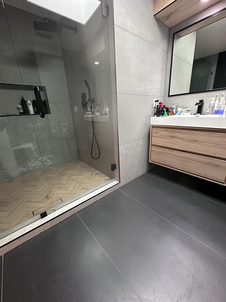 Modern bathroom with a glass shower, wooden vanity, and gray walls.