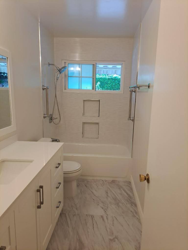 Bright bathroom: white vanity, marble floor, shower with glass door, and small window.