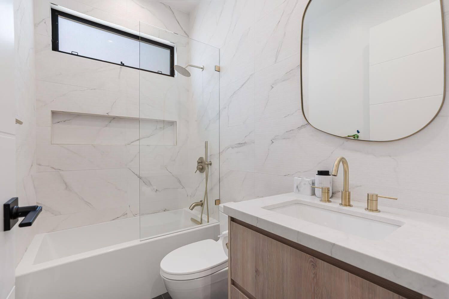 Modern bathroom with white marble walls, gold fixtures, and a wooden vanity.
