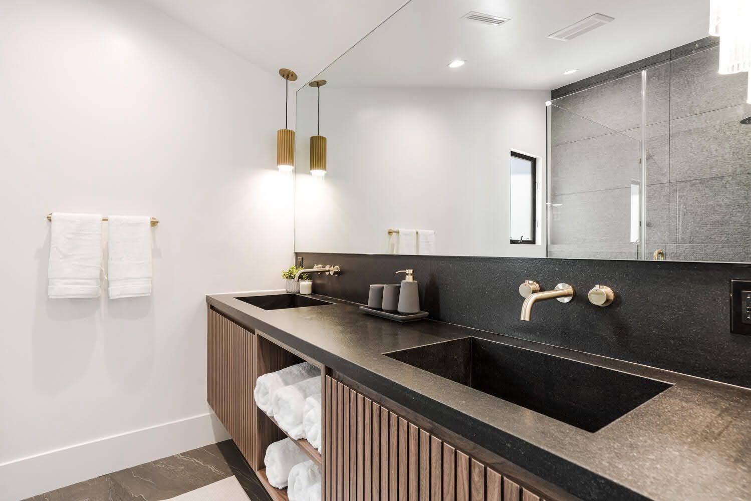 Modern bathroom with dark countertop, wooden vanity, and gold fixtures.