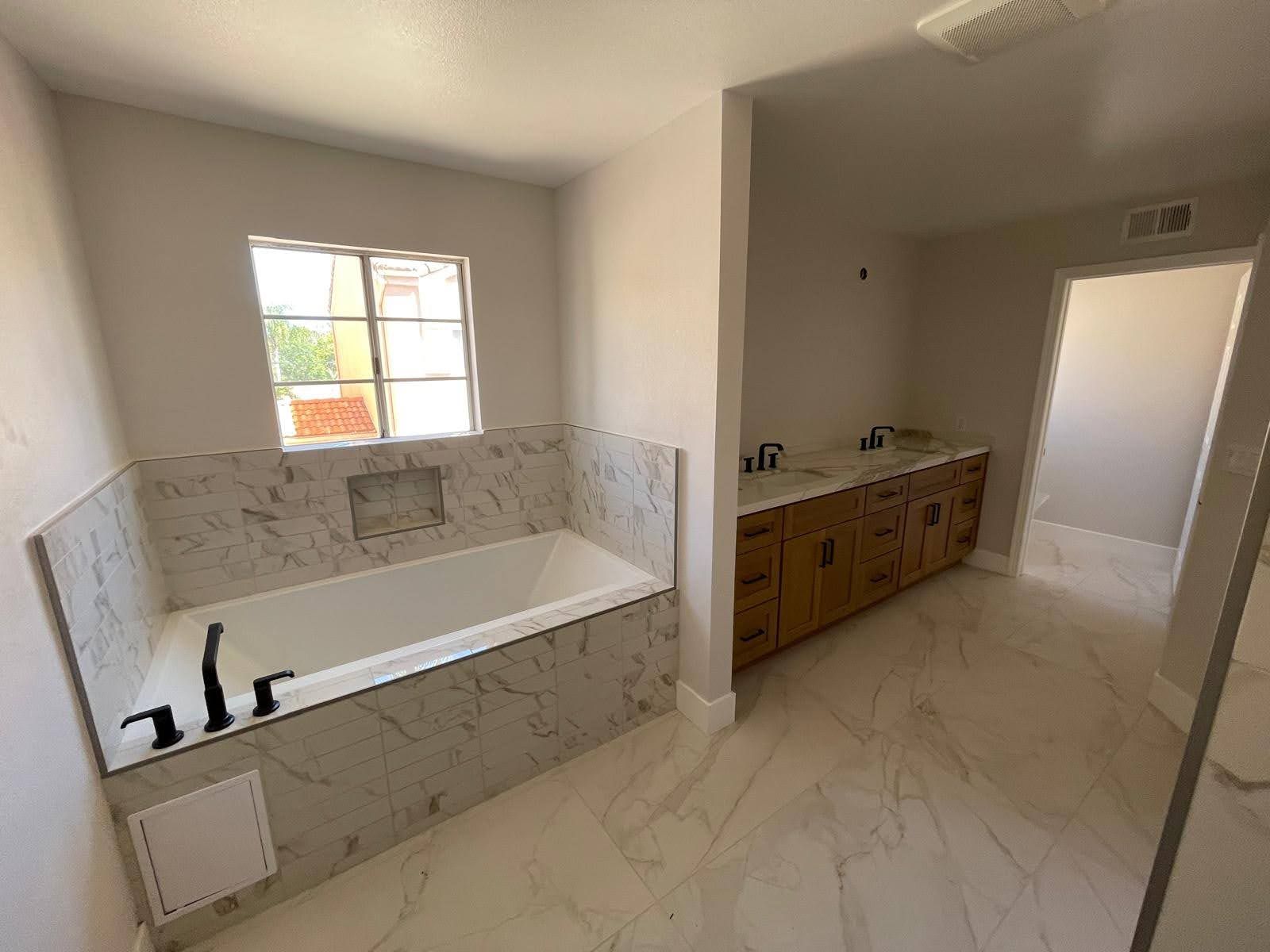 A newly renovated bathroom with a tub, vanity, and marble-look tile.