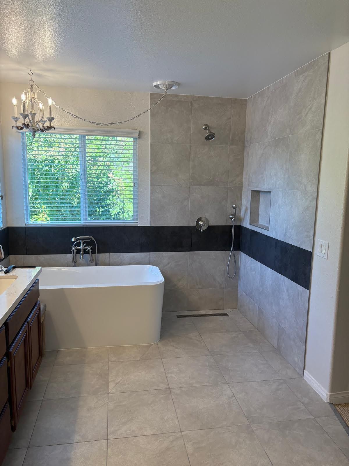 Bathroom with freestanding tub, shower with gray and black tile, and a window.