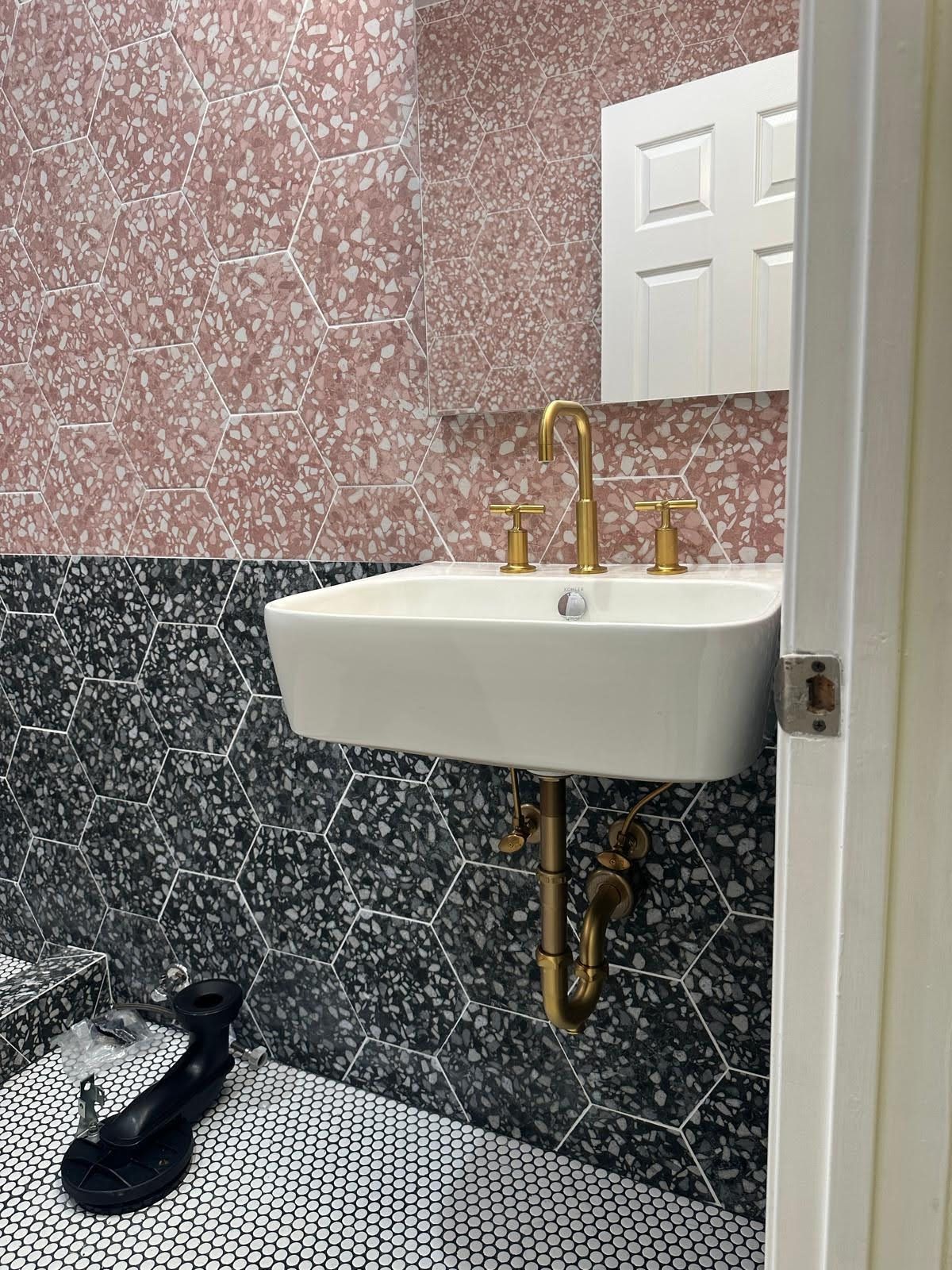 Bathroom with pink/black patterned walls, white sink, gold faucet, and black water fountain.