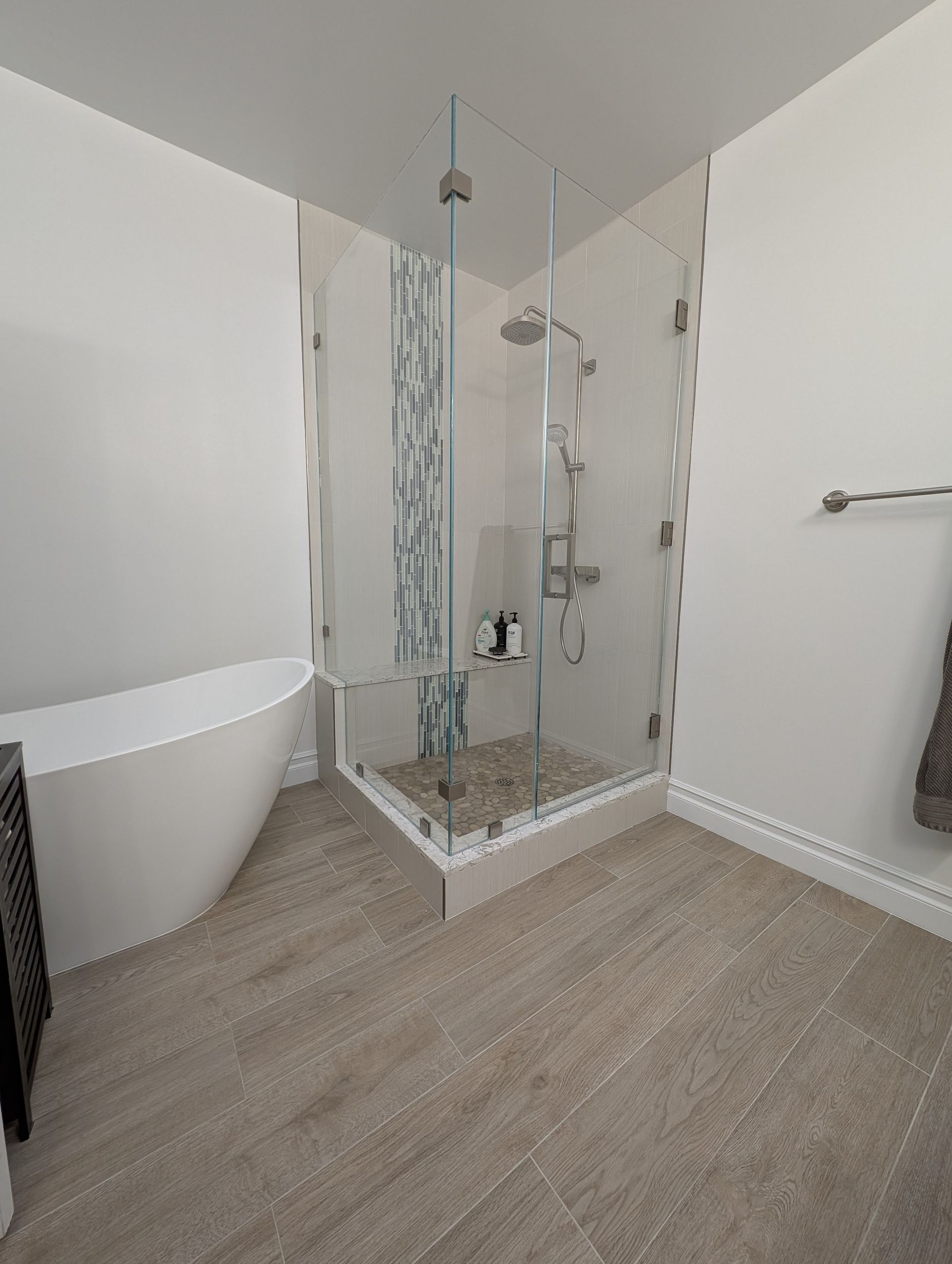 Modern bathroom with glass shower, white tub, and neutral-toned tile flooring.