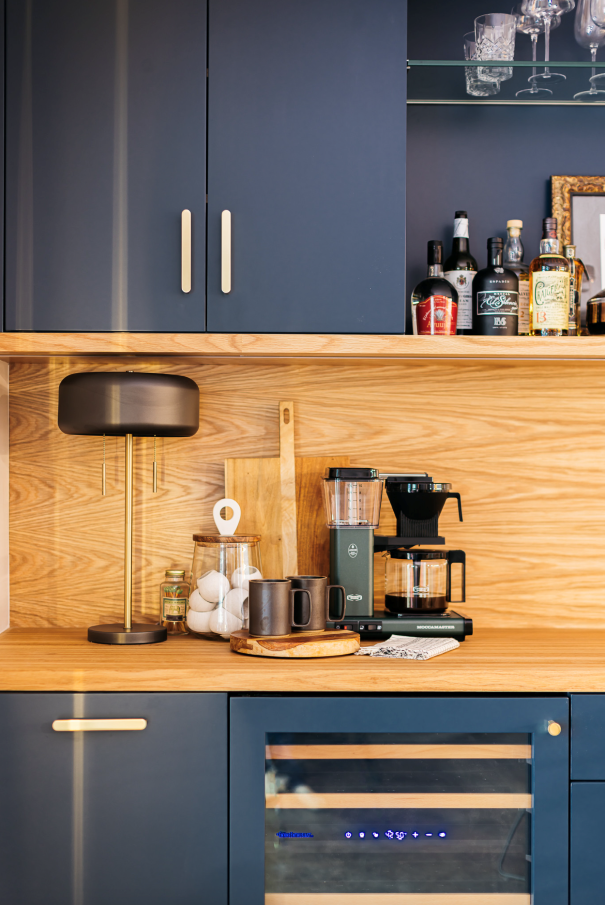 A coffee bar with a navy blue cabinet, wooden shelf and countertop, and a wine cooler.