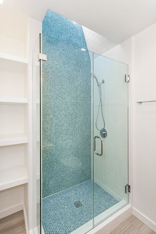 Shower with blue mosaic tile wall and floor, glass door, and white shelving.