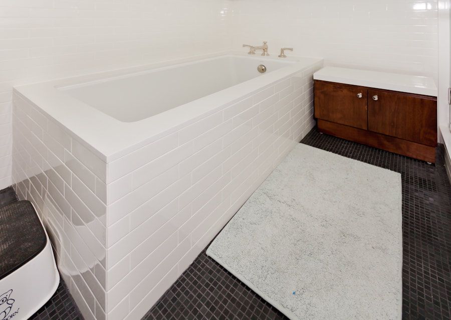 Bathroom with a white tub, dark floor, and wooden cabinet. A gray bath mat sits on the floor.