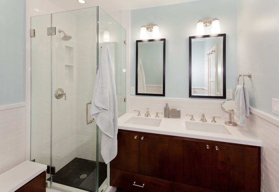 Modern bathroom with a glass shower, dark wood vanity, and two mirrors on a light blue wall.
