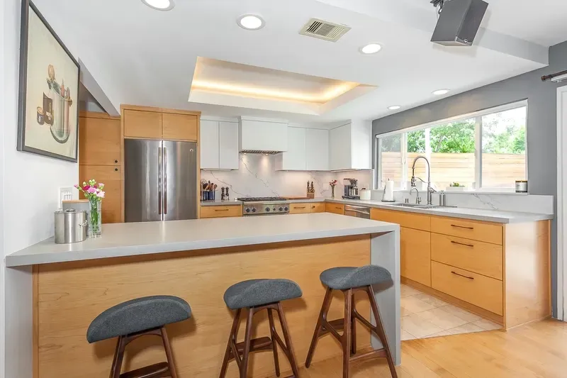 Modern kitchen with wood cabinets, gray countertops, and three bar stools.