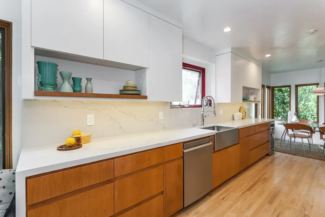 Modern kitchen with white cabinets, wooden lowers, stainless steel appliances, and light countertops.