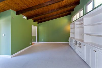 Green-walled room with wooden beams, built-in white shelves, and light carpet.