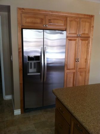 Refrigerator built into wooden cabinetry with cabinets on the sides; kitchen.