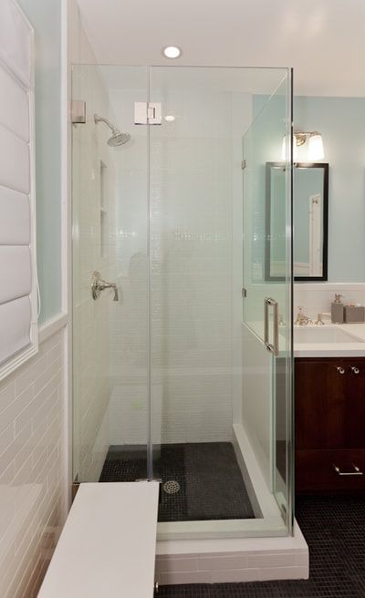 Modern bathroom with a glass shower enclosure, white bench, and dark floor.