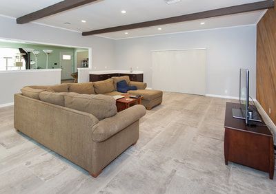 Spacious living room with gray tile floor, sectional sofa, TV, and dark wood beams.