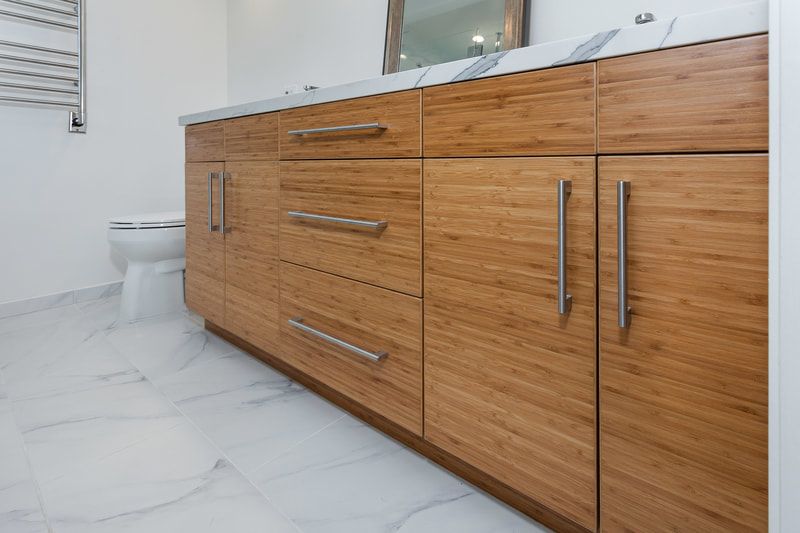 Wooden bathroom vanity with silver handles, white countertop, and marble floor.