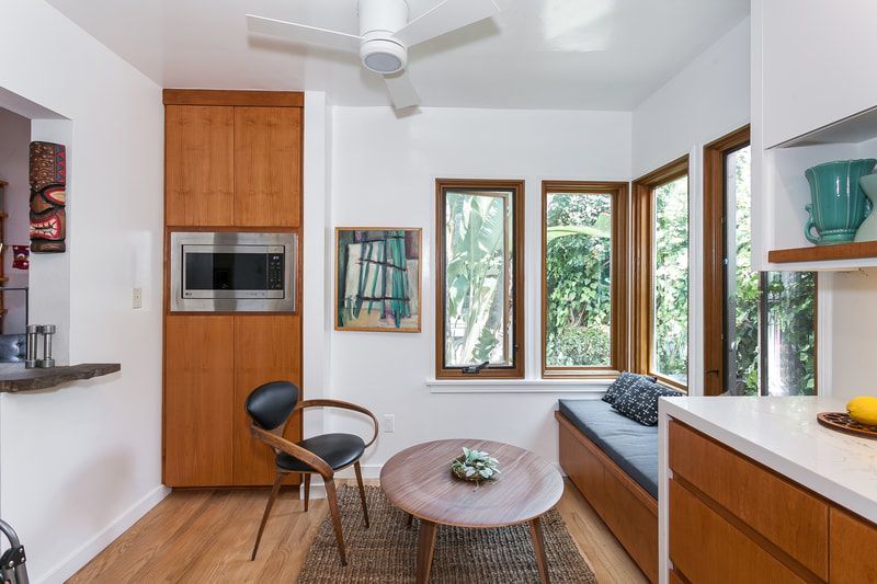 Cozy kitchen nook with built-in seating by windows, wooden cabinetry, a small table, and a black chair.