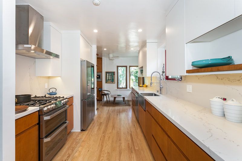 Modern, galley kitchen with wood cabinets, stainless steel appliances, and white countertops.