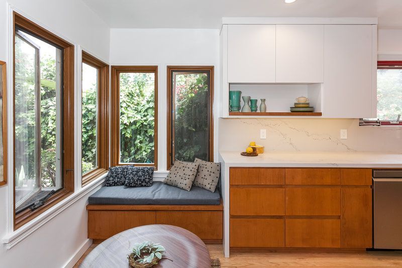 Kitchen with window seat, wooden cabinets, and white countertops; natural light fills the space.