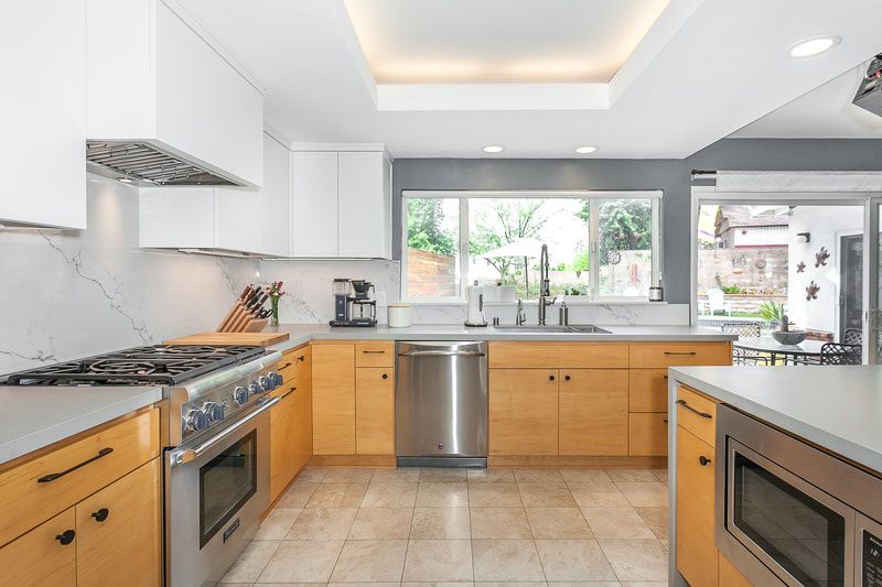 Modern kitchen with light wood cabinets, stainless steel appliances, and white countertops.