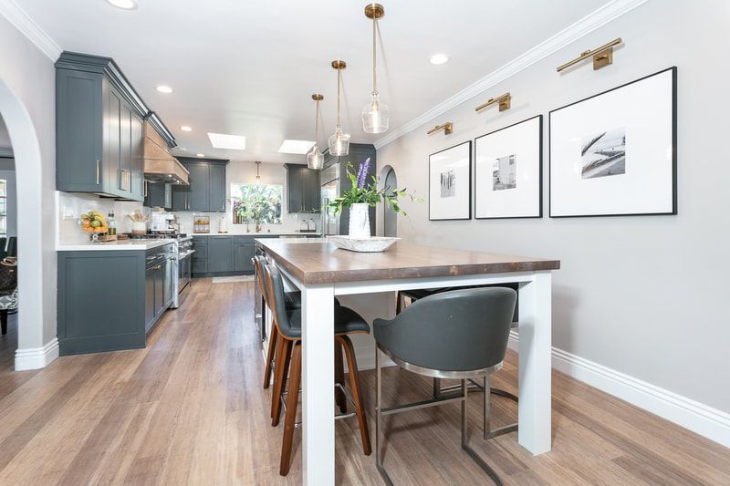 Modern kitchen with gray cabinets, island table, and three framed photos on a light gray wall.
