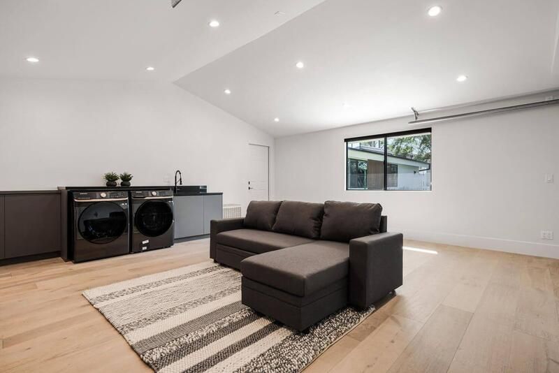 Laundry room with gray washer/dryer, couch, sink, rug, and window.