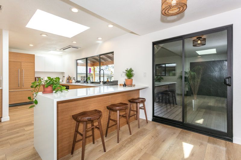 Modern kitchen with wood accents, white countertops, and island with three stools, with large sliding glass door.