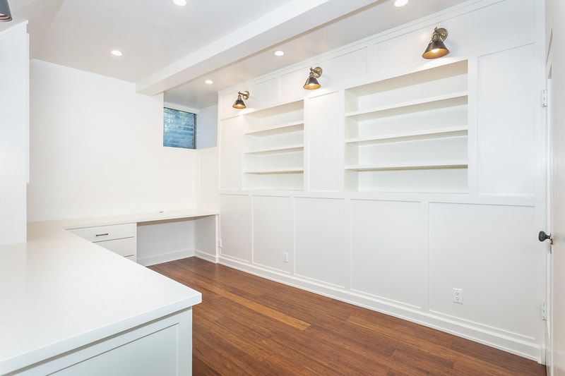 White office space with built-in shelves, desk, wooden floors, and recessed lighting.