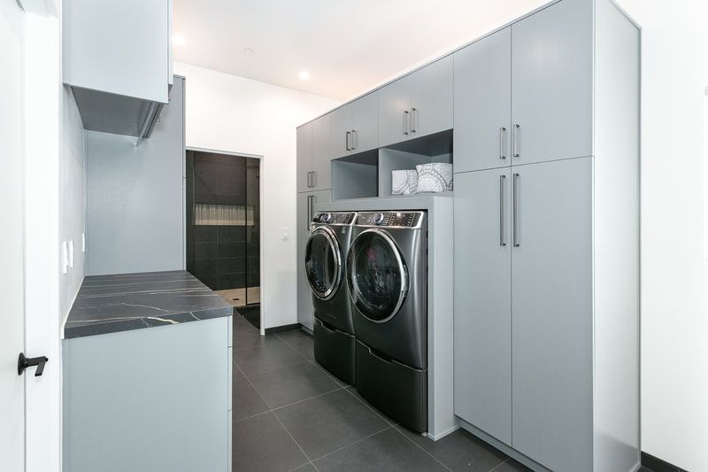 Modern laundry room with gray cabinets, dark countertops, and stainless steel washer and dryer.