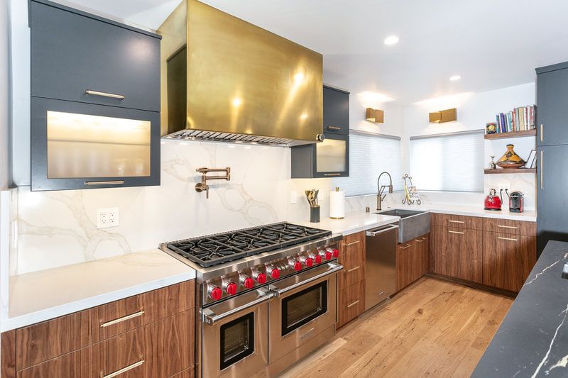 Modern kitchen with gold range hood, navy cabinets, and wood accents.