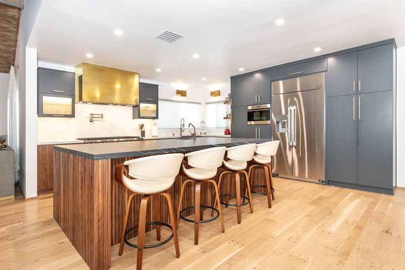 Modern kitchen with gray cabinets, wood island, gold range hood, and stainless steel appliances.