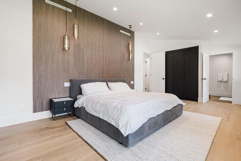 Bedroom with gray bed, white bedding, wooden floors, accent wall, and modern light fixtures.