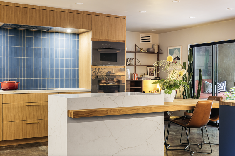 Modern kitchen with blue tile backsplash, wood cabinets, and marble island with a wood countertop.