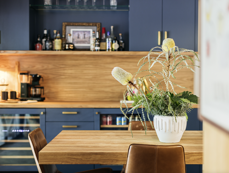 A kitchen with a wooden table, blue cabinets, and a potted plant with yellow flowers.