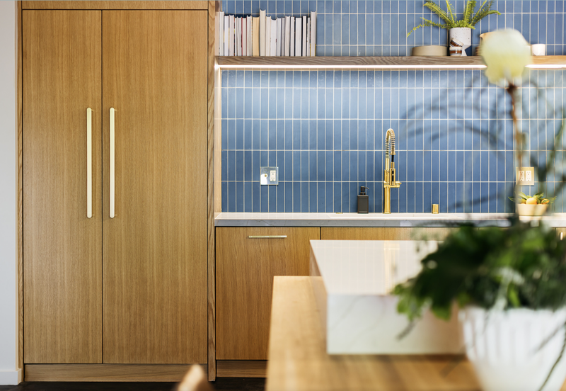 Wooden kitchen cabinets with gold hardware, blue tile backsplash, and gold faucet.