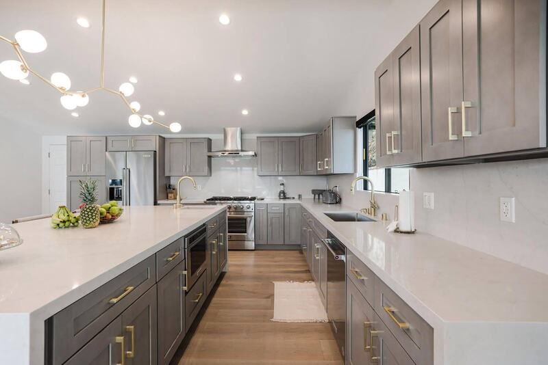 Modern gray kitchen with white countertops, wooden floors, and gold hardware.